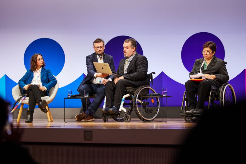 Soufiane on stage of Regional Disability Summit, me holding his laptop
