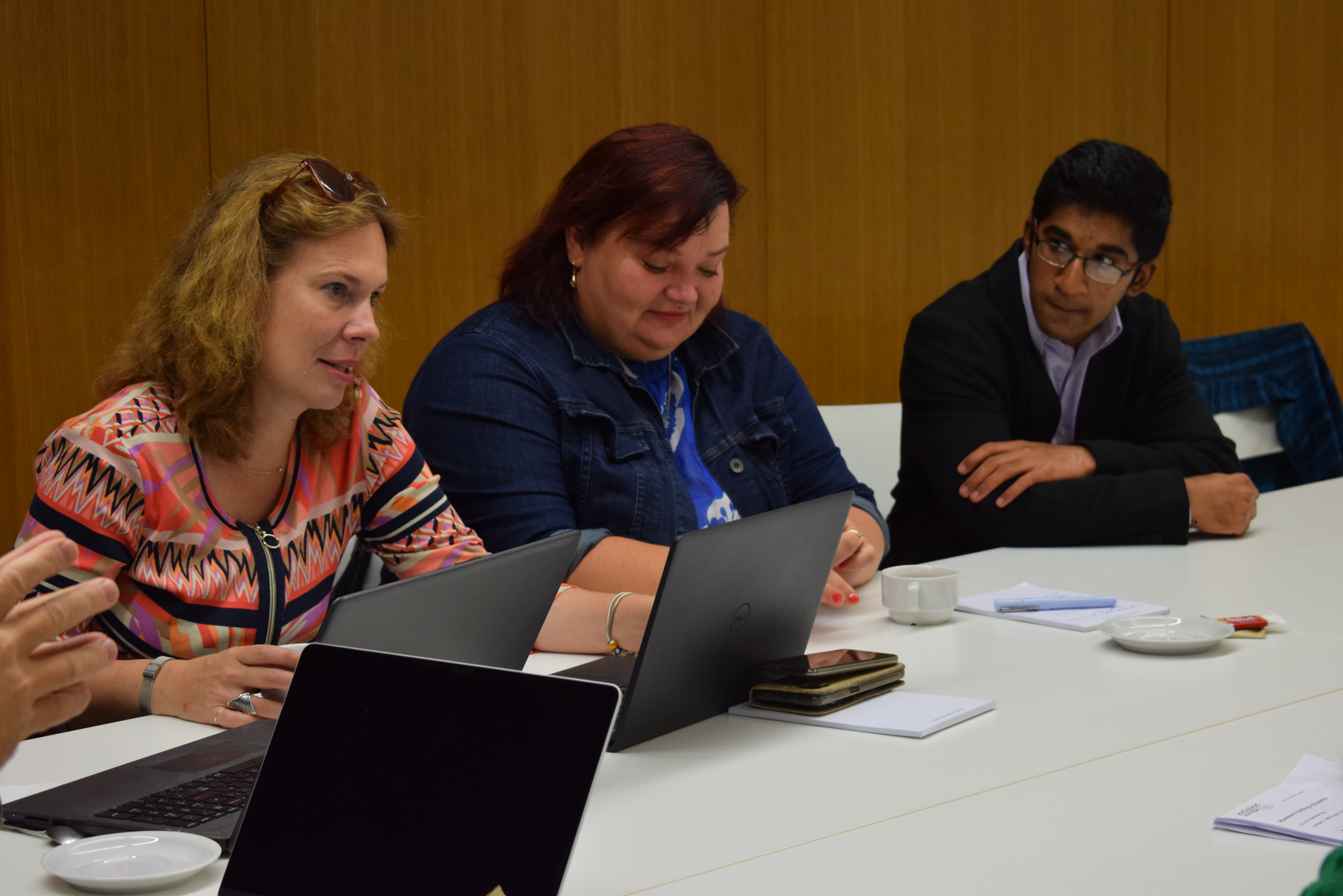 Three participants sitting in front of the table; one of them is speaking and the rest are looking at her with attention